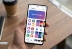 Hand holding samsung galaxy phone showing one ui themes section in galaxy theme store with colorful app icons and theme wallpapers on wooden desk background